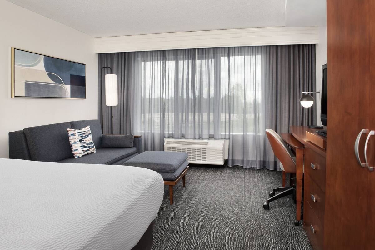 A hotel room with a large bed, a sofa, a desk, and a television.