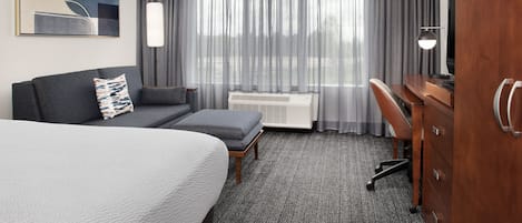 A hotel room with a large bed, a sofa, a desk, and a television.