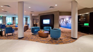 A modern lobby with blue armchairs, a round coffee table, and a large screen.