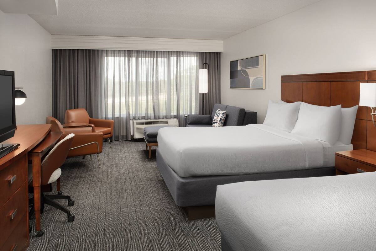 A hotel room with a large bed, a desk, a chair, and a TV.