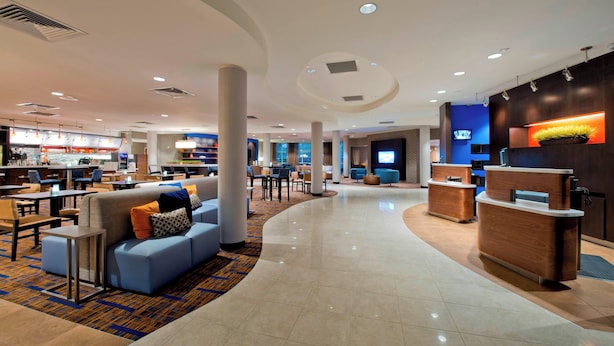 A modern hotel lobby with a curved reception desk, seating areas, and a bar.