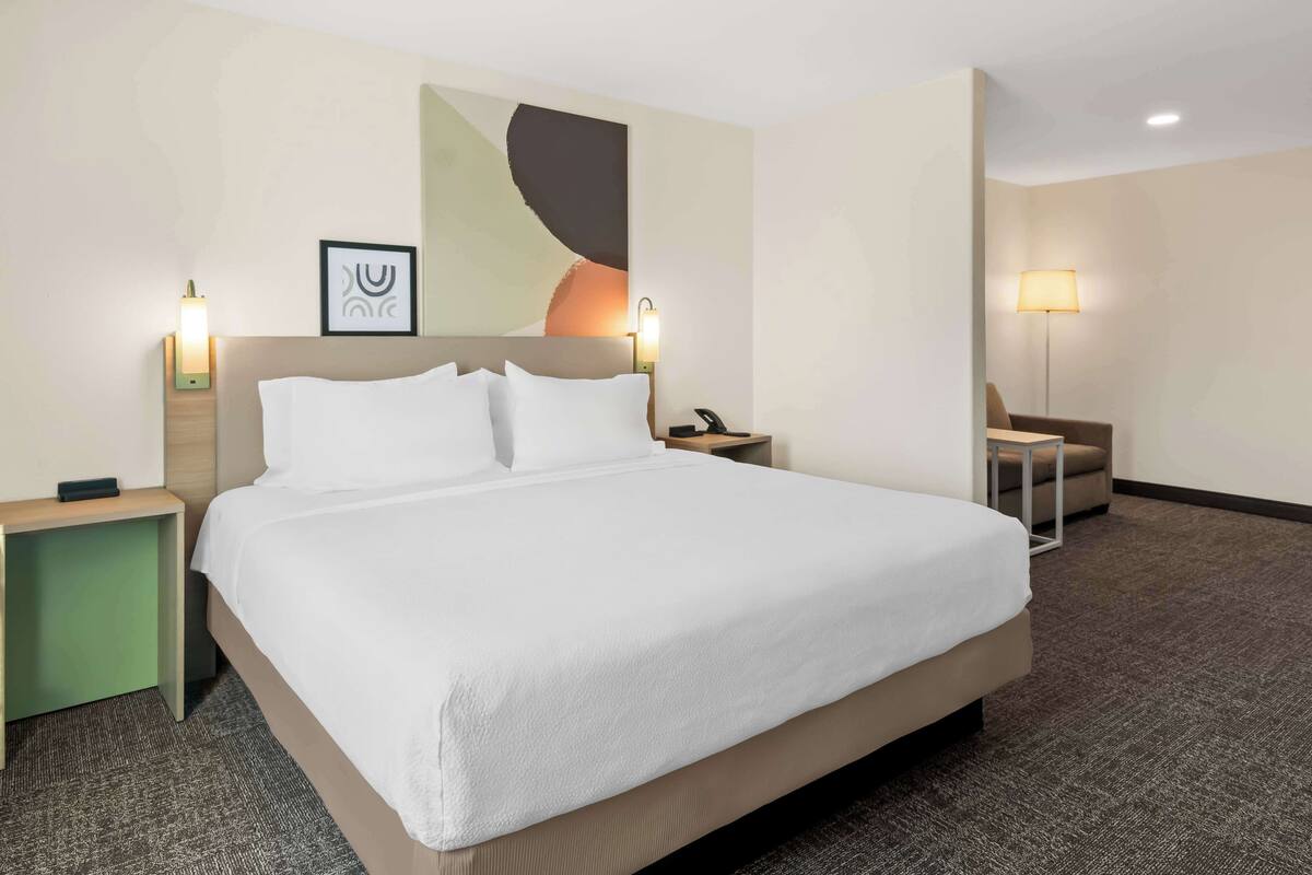 A hotel room with a large bed, two bedside tables, a chair, a desk, and a wall-mounted lamp.