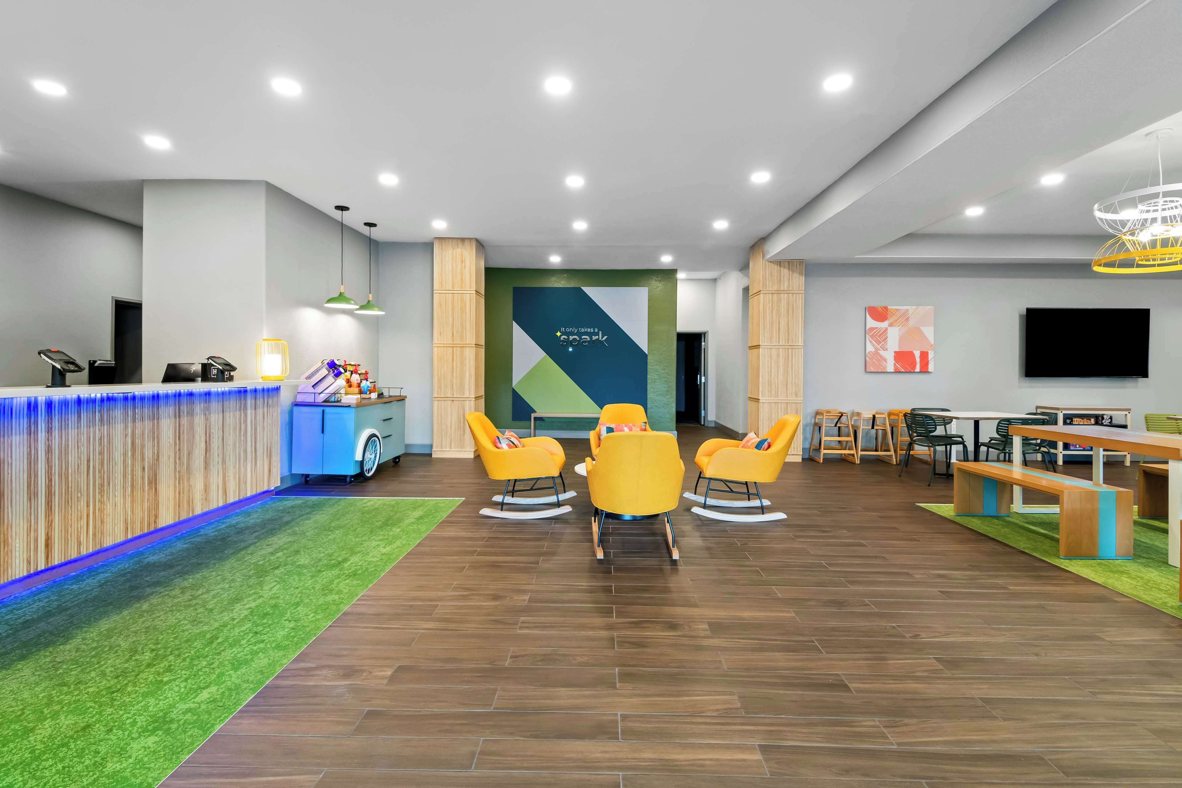 A modern reception area with a wooden reception desk, a green carpet, and yellow chairs.
