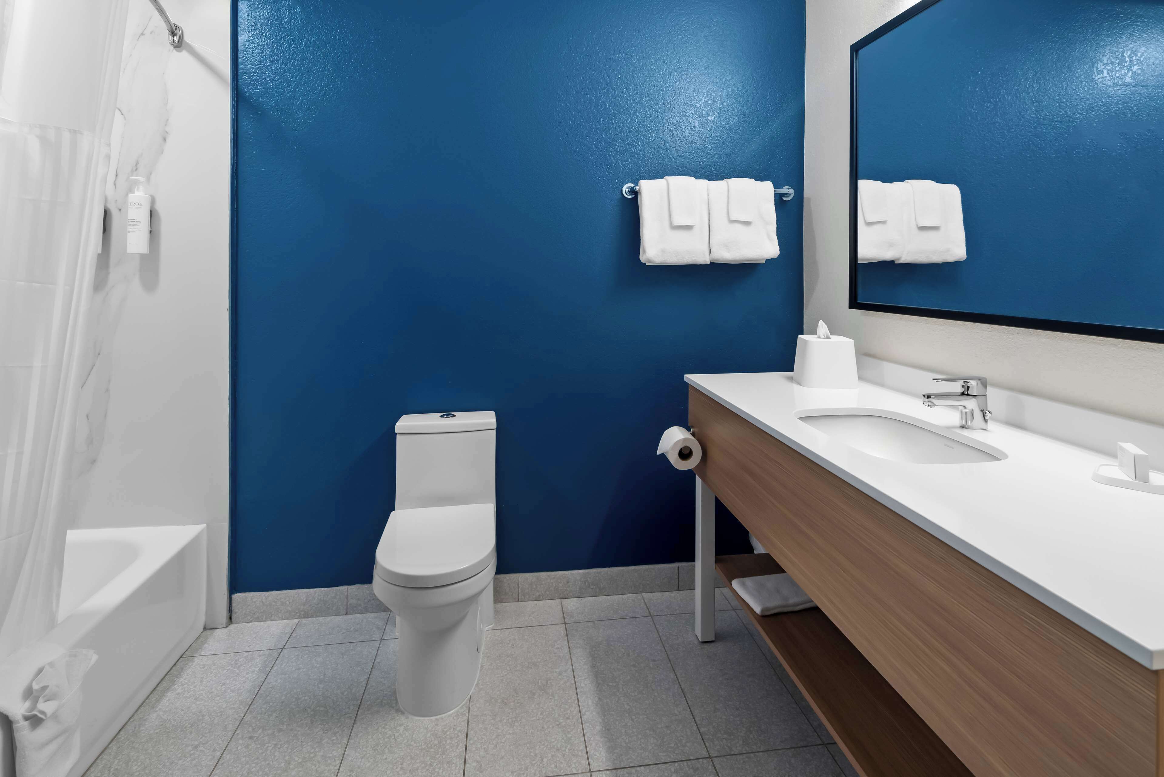 Un baño moderno con una pared azul de acento, un inodoro blanco, un lavabo con espejo y un perchero para toallas.