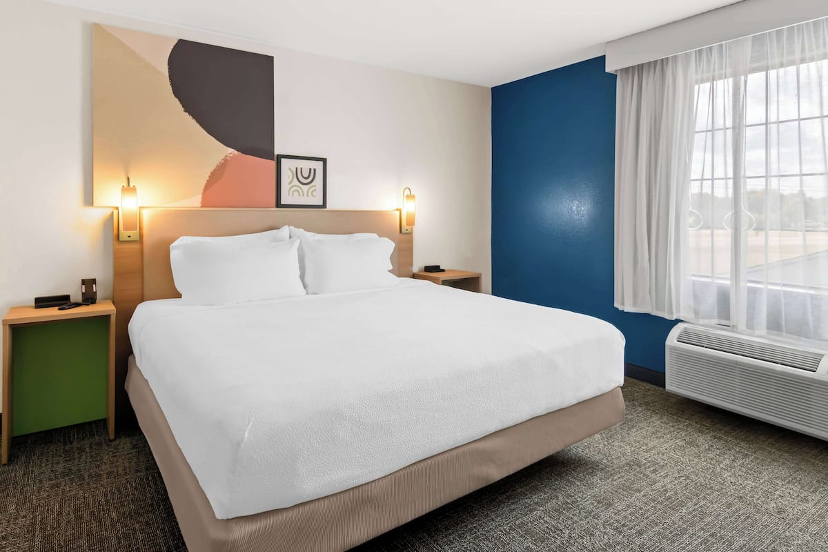 A hotel room with a large bed, two bedside tables, a wall-mounted artwork, and a window with curtains.