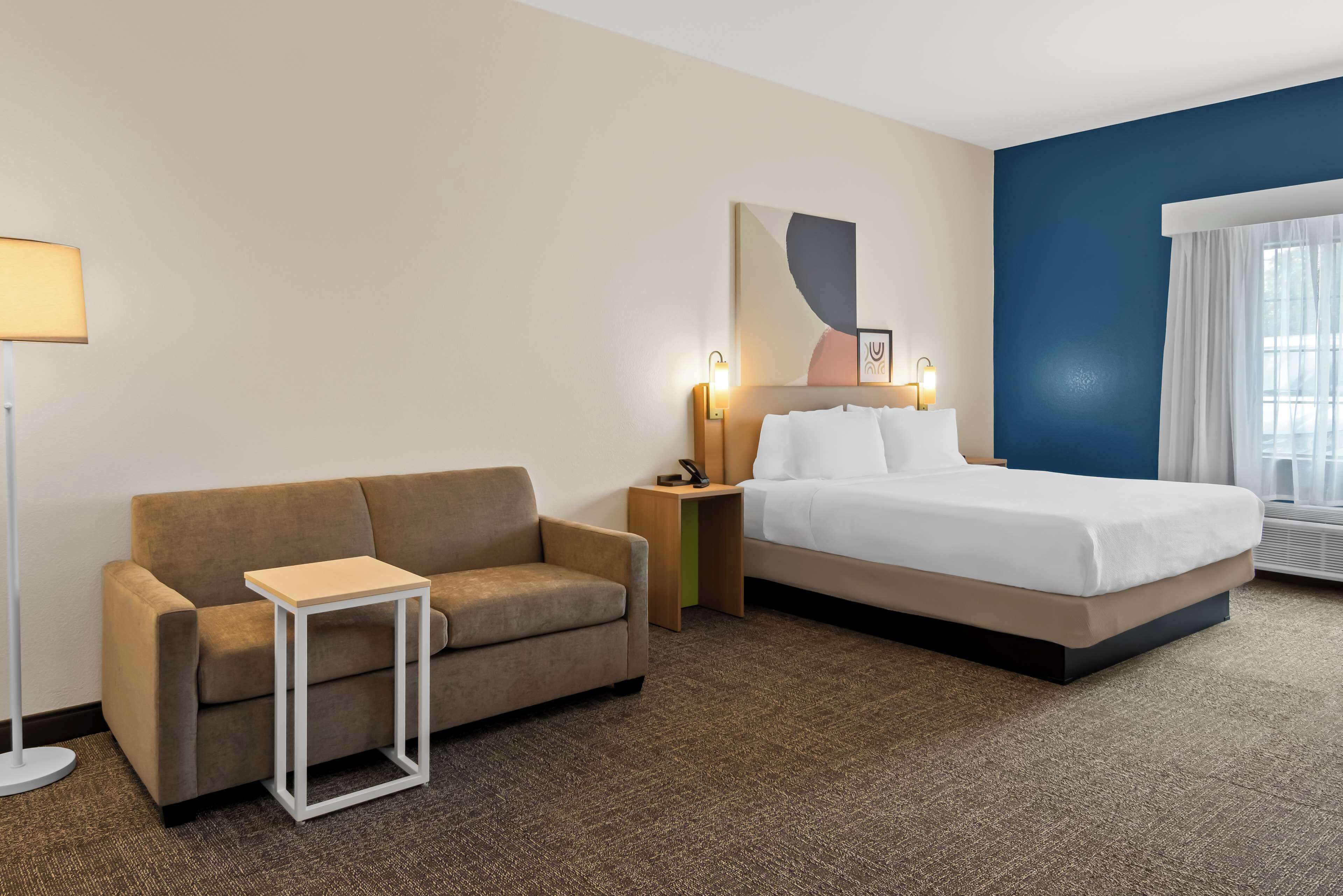 A hotel room with a bed, a sofa, a small table, a nightstand, and a lamp.
