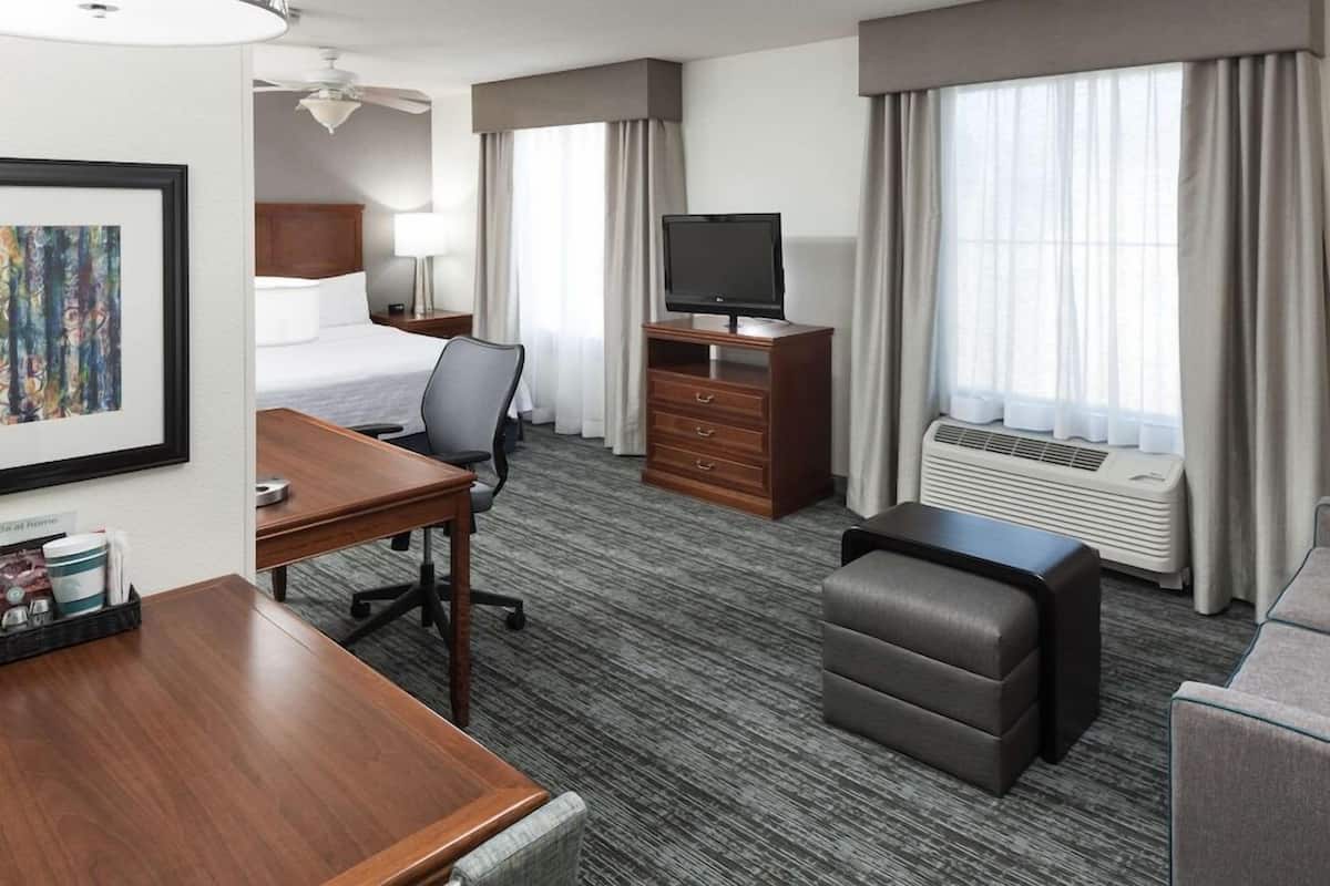 A hotel room with a bed, desk, chair, television, dresser, and air conditioning unit.
