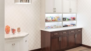 A kitchen with white cabinets, a marble countertop, and a built-in shelf with snacks and condiments. - Homewood Suites by Hilton El Paso Airport (El Paso)