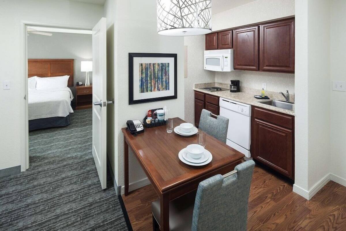A hotel room with a wooden dining table, a microwave, and a small kitchen area.