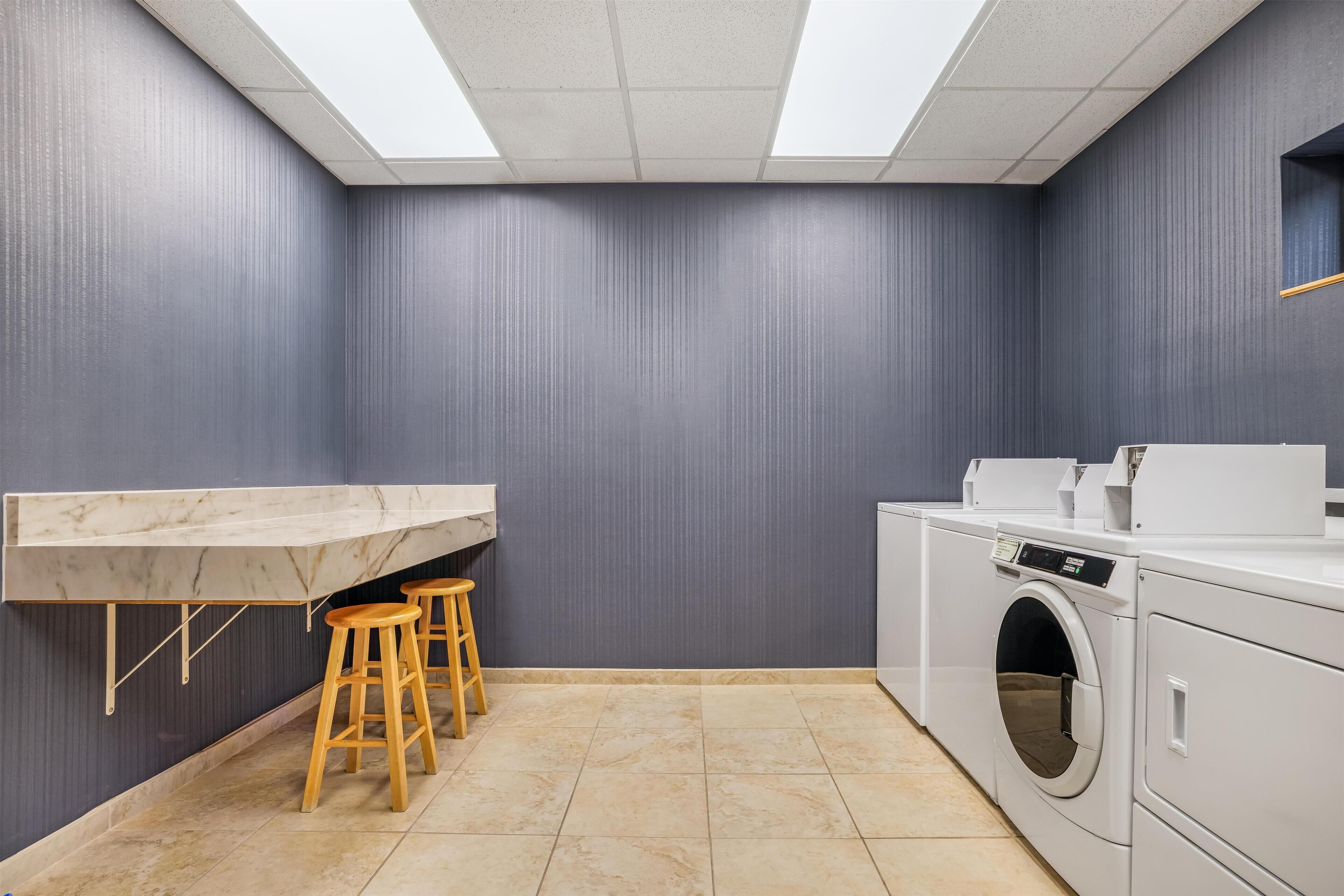 Une buanderie avec un plan de travail en marbre, des tabourets en bois, un lave-linge et un luminaire suspendu au plafond.