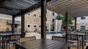 An outdoor patio area with tables and chairs, a stone building in the background, and a pool. - Homewood Suites by Hilton Dallas-Frisco (Frisco)