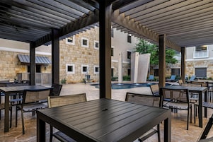 Un patio al aire libre con mesas y sillas, un edificio de piedra al fondo y una piscina.
