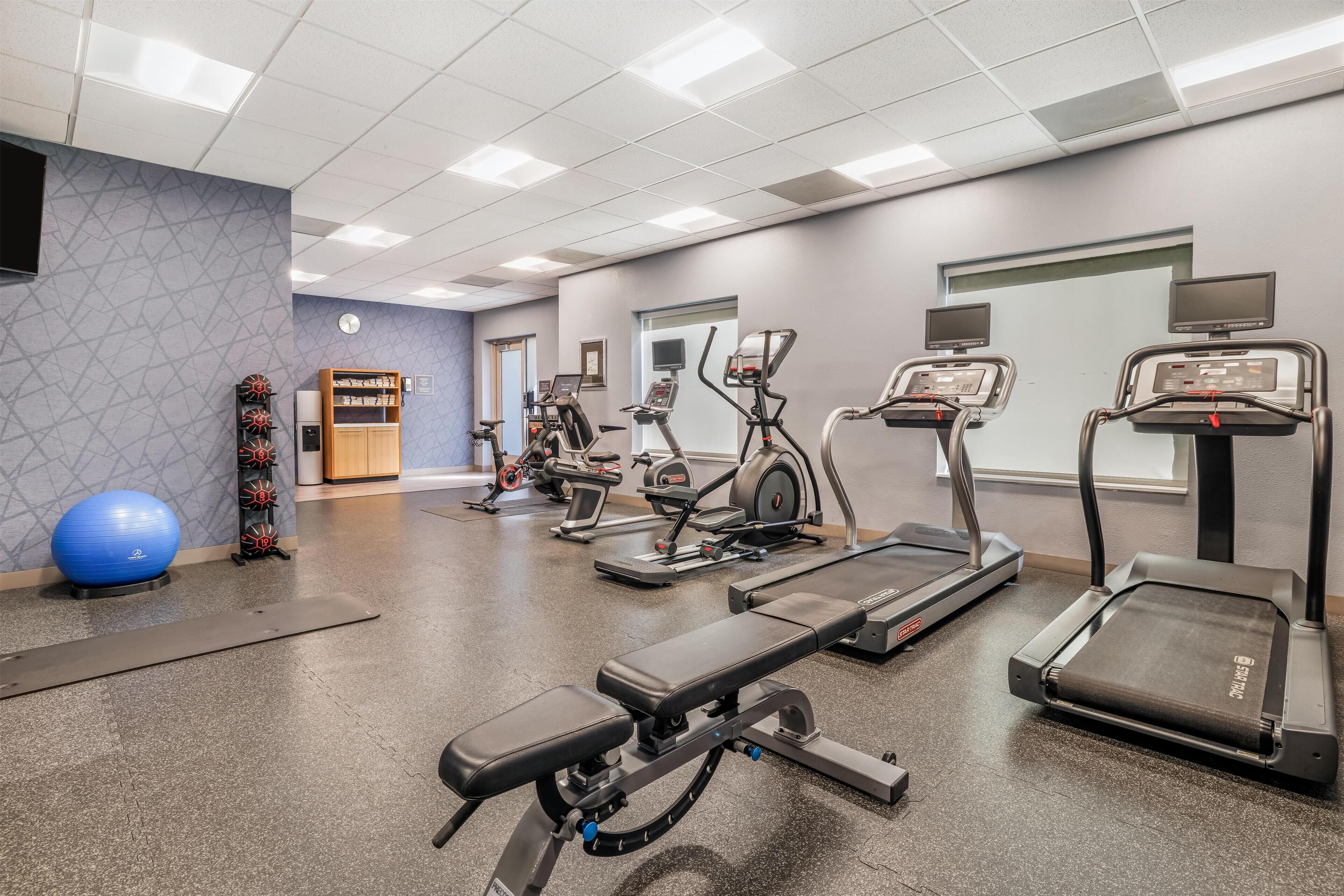 Une salle de sport équipée de tapis de course, de vélos elliptiques, d’un vélo d’appartement et d’un rameur.