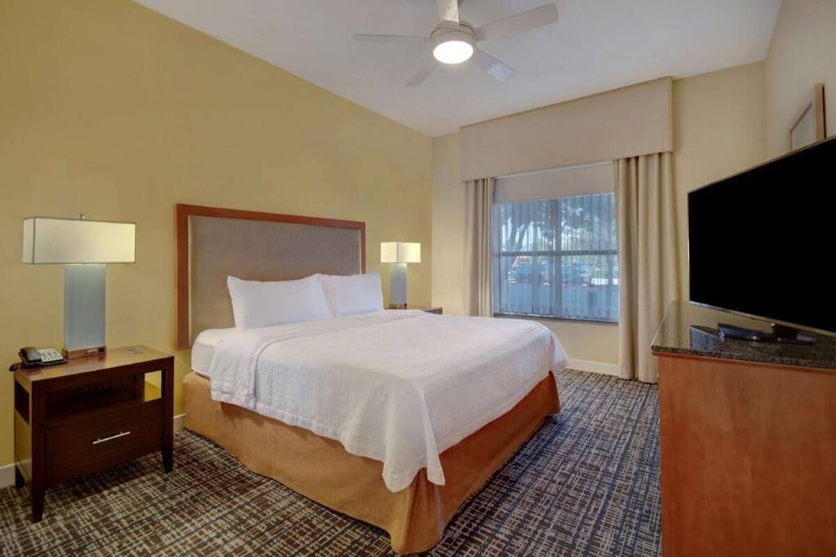 Une chambre d’hôtel avec un lit, une table de chevet, un téléviseur et une fenêtre avec des rideaux.