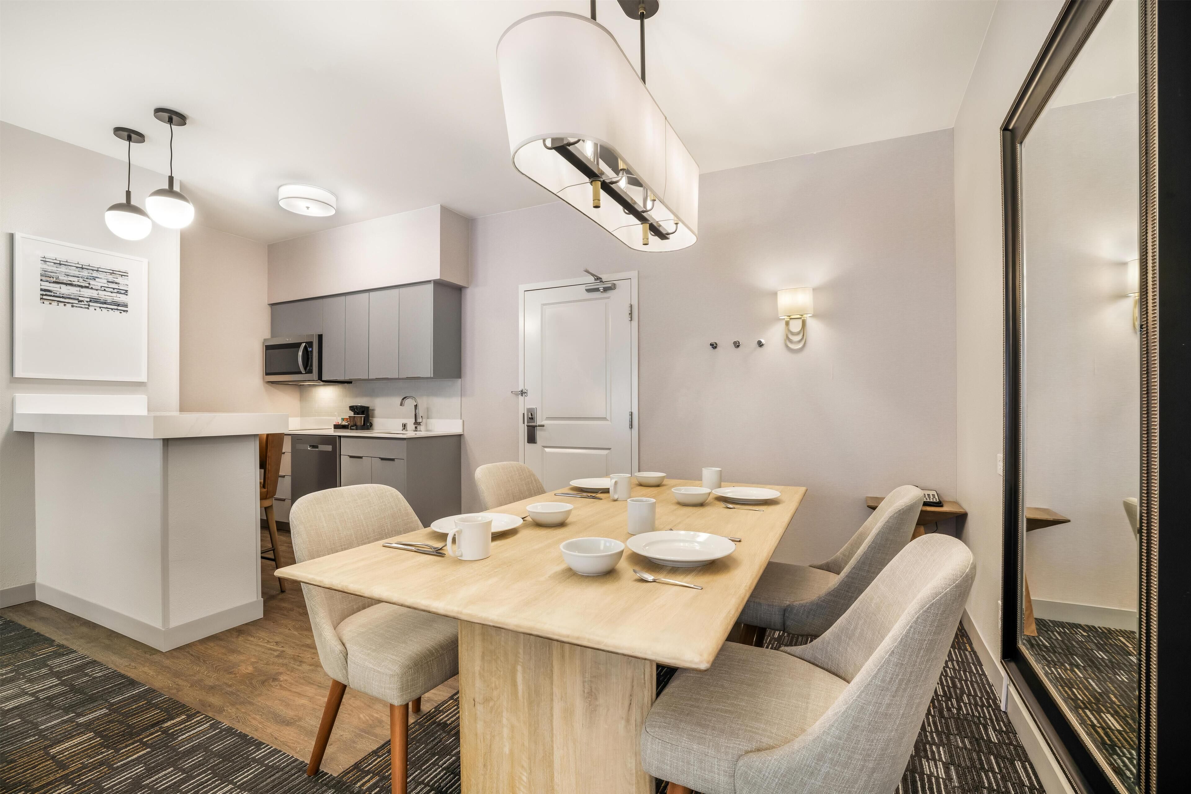 Ein moderner Hotel-Speisebereich mit Holztisch, grau gepolsterten Stühlen und einer Küche im Hintergrund.