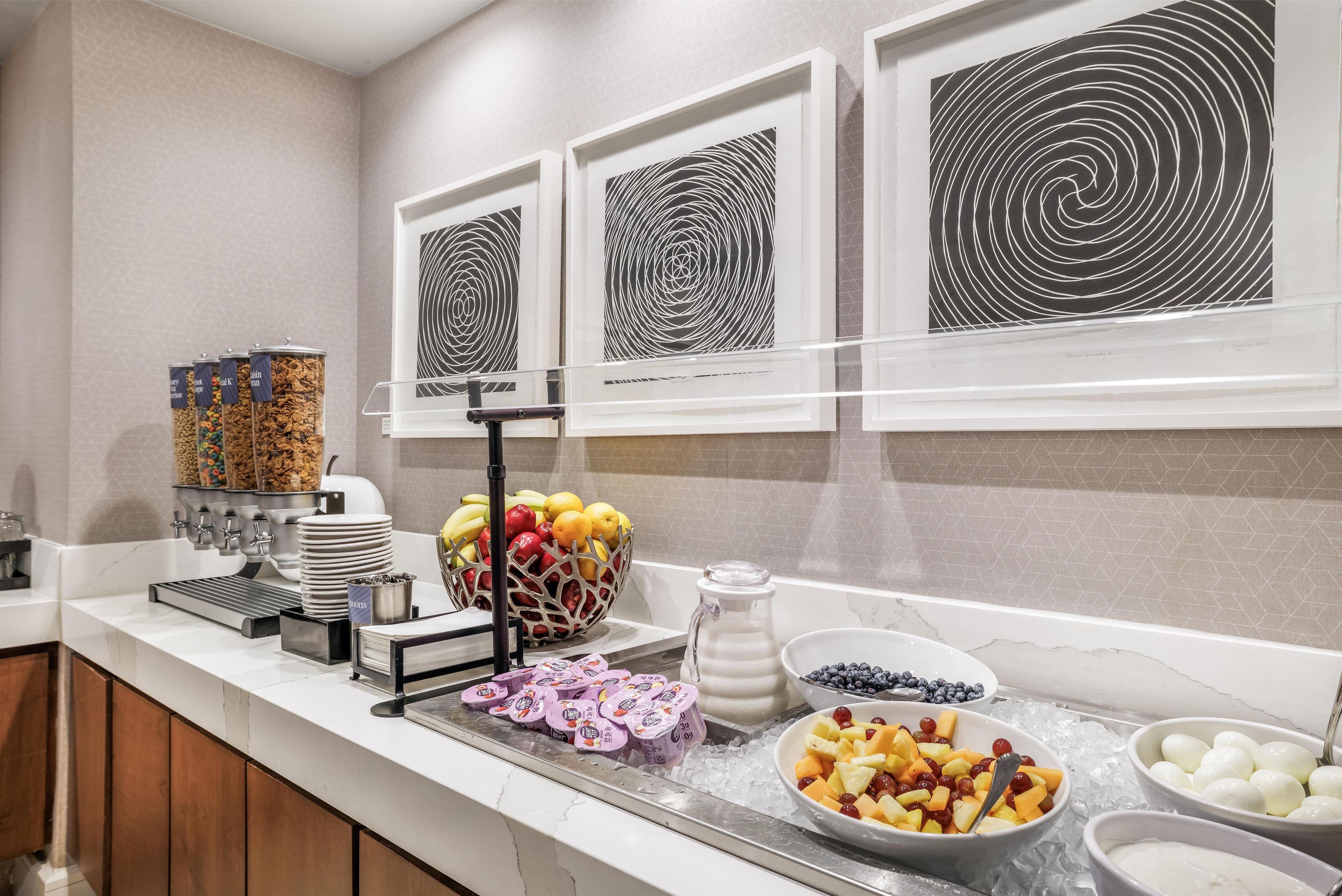 Uma área de buffet com diversos alimentos, um dispensador de suco e uma máquina de café.