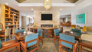 A modern living room with a fireplace, bookshelves, a television, and a dining area. - Homewood Suites by Hilton Dallas-Frisco (Frisco)