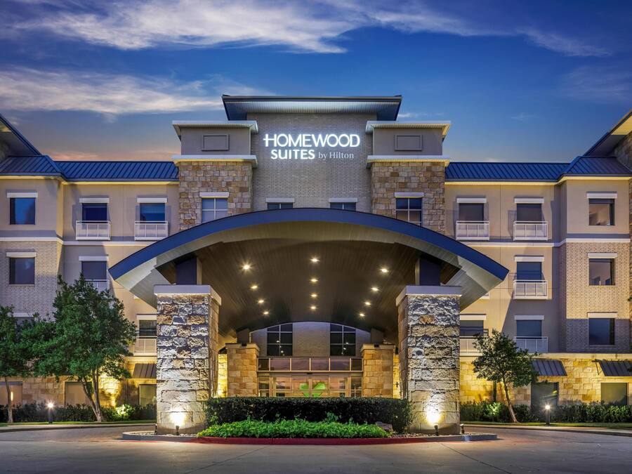 A hotel entrance with a stone facade, multiple balconies, and a clear sky.
