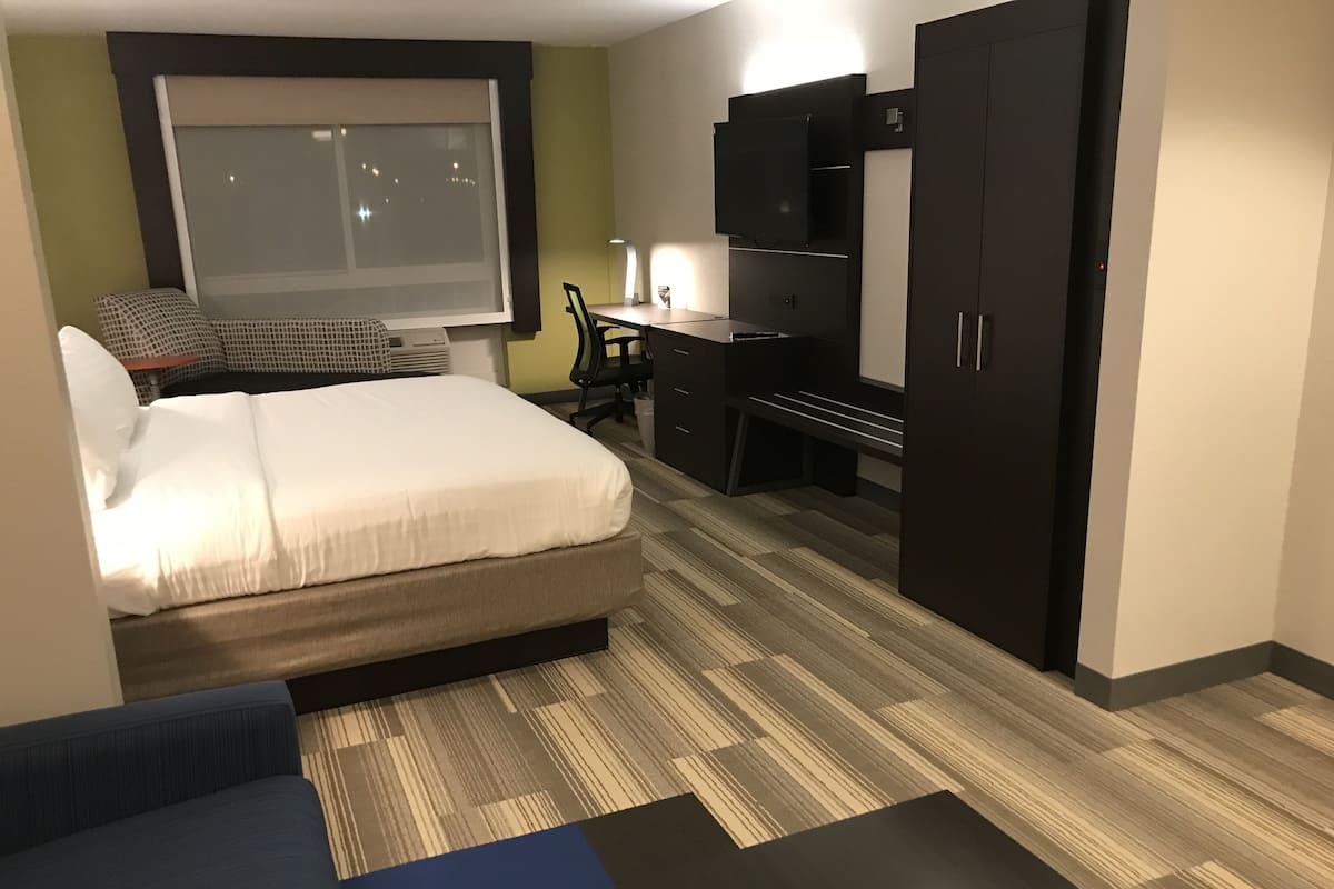 A hotel room with a bed, a desk, a wardrobe, and a TV.