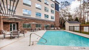 Una piscina con escalera metálica, rodeada de asientos exteriores y un edificio con varias ventanas.