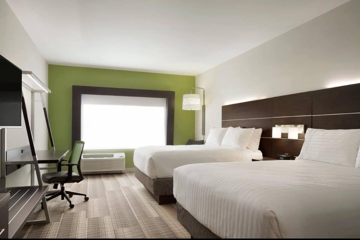 A hotel room with two beds, a desk, a chair, a TV, and a large window.