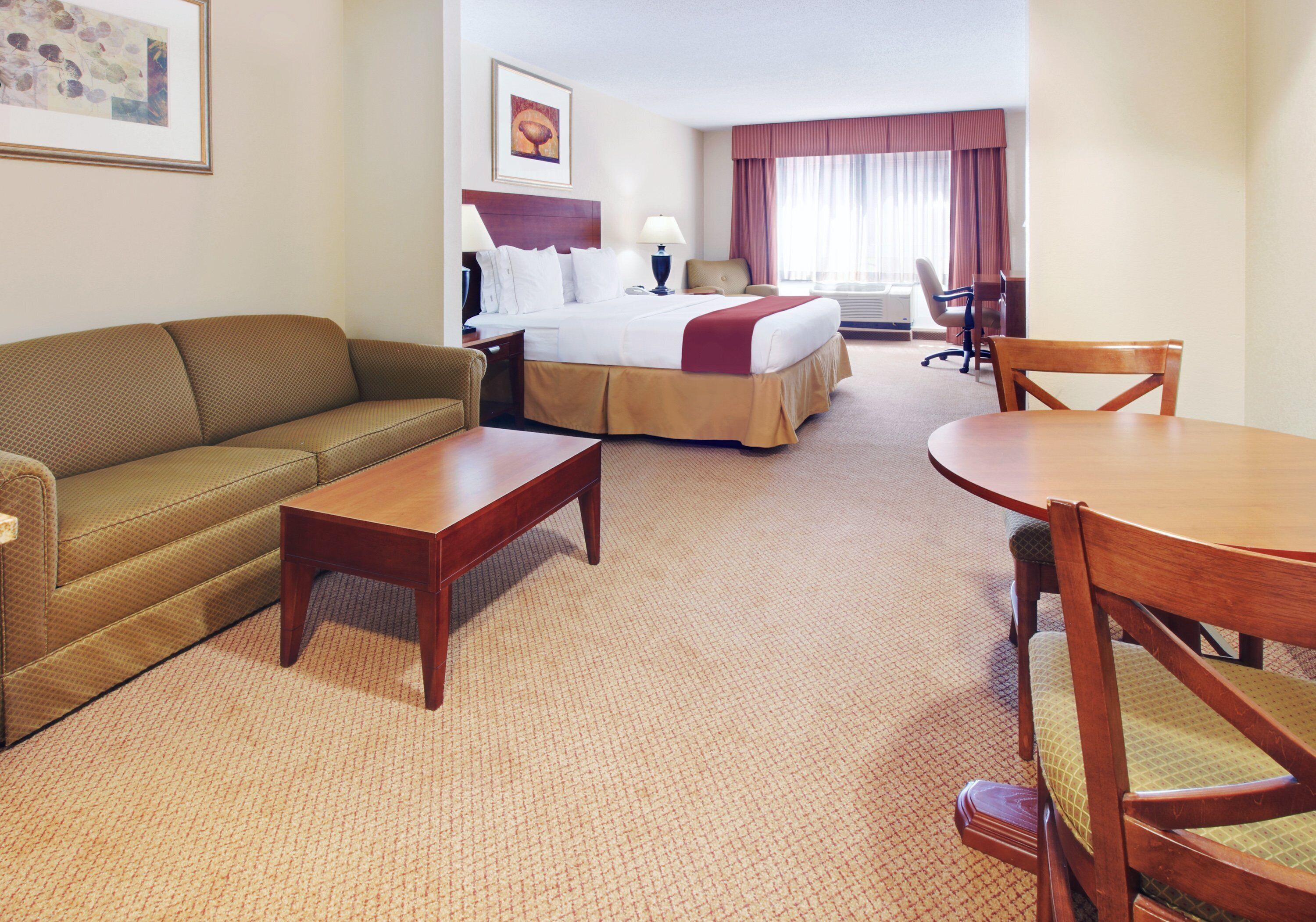 A hotel room with a bed, a sofa, a dining table, and a chair.