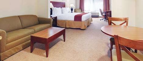 A hotel room with a bed, a sofa, a dining table, and a chair.