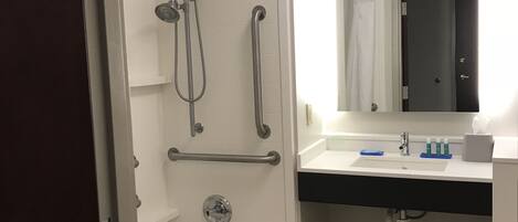 Un baño moderno con cabina de ducha, barras de apoyo, bañera, lavamanos con espejo e inodoro.