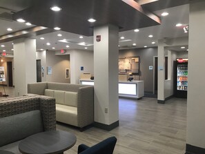 Un hall d’hôtel comprenant des espaces de détente, un comptoir d’accueil et un distributeur automatique.