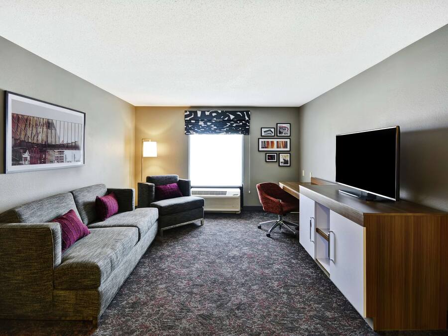 A compact hotel room with a sofa, a desk, a chair, and a TV.