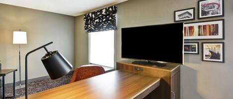 Een hotelkamer met een houten bureau, een televisie, een lamp, een stoel en lijstjes met foto's aan de muur.