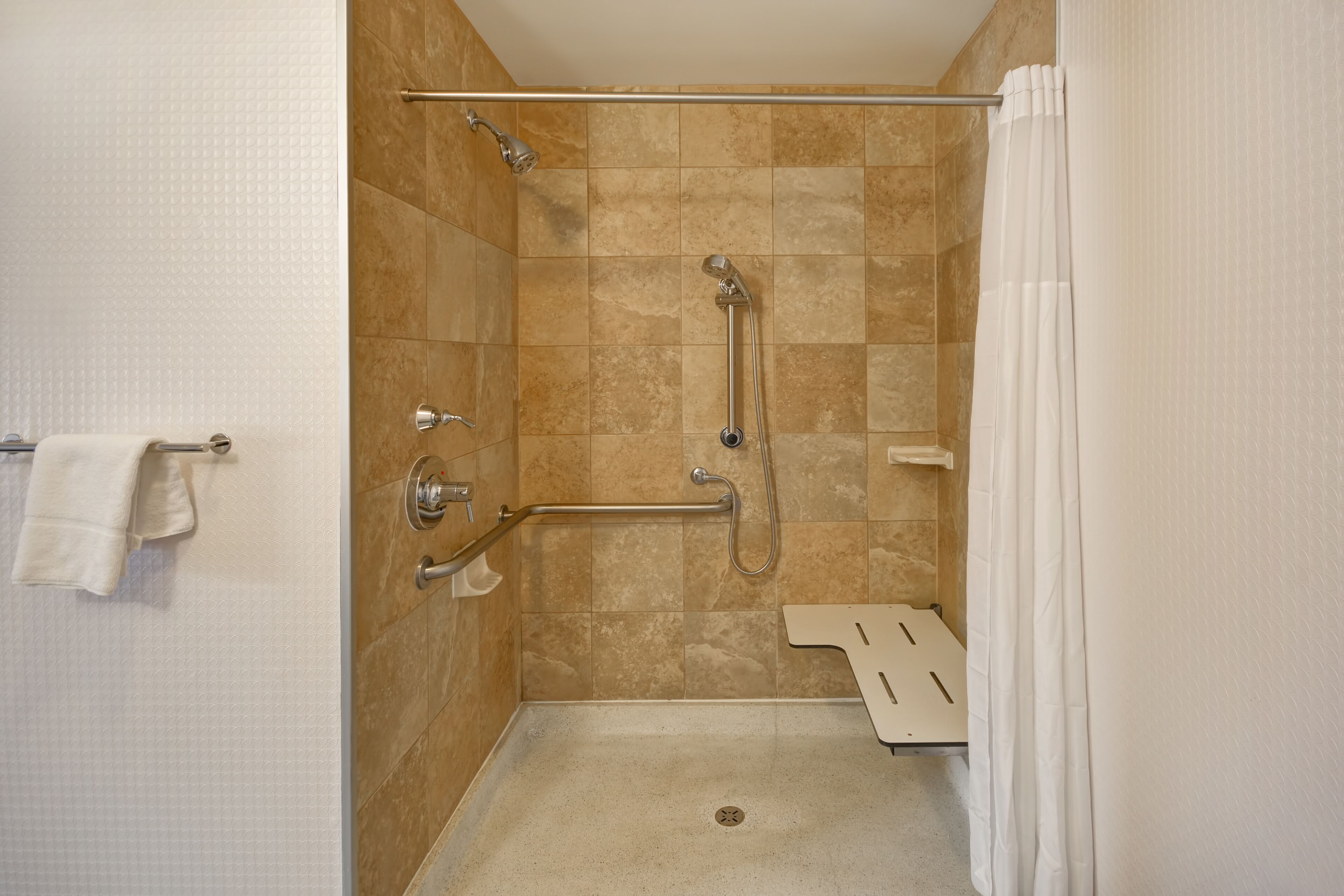 A shower with a grab bar, a handheld showerhead, and a handheld faucet.