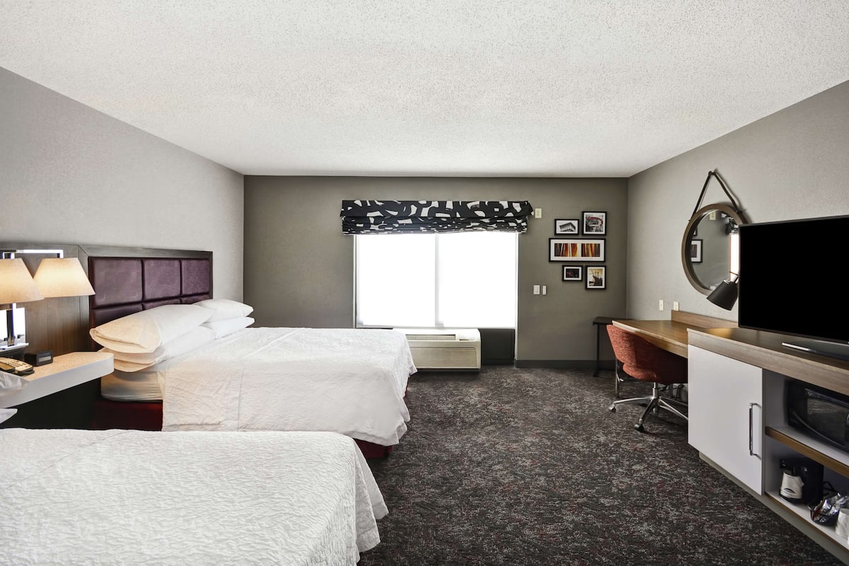 A hotel room with two beds, a desk, a TV, and a mirror.