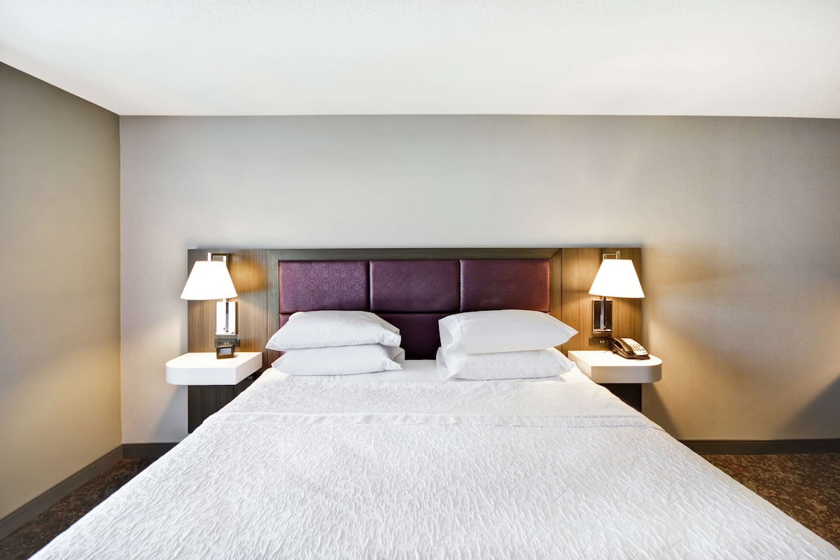 A hotel room with a large bed, two bedside tables with lamps, and a headboard with a built-in shelf.