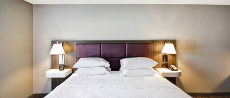 A hotel room with a large bed, two bedside tables with lamps, and a headboard with a built-in shelf.