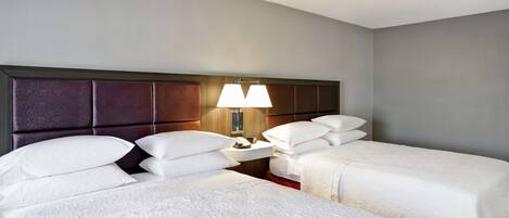 A hotel room with two beds, a nightstand with a lamp, and a wall-mounted phone.