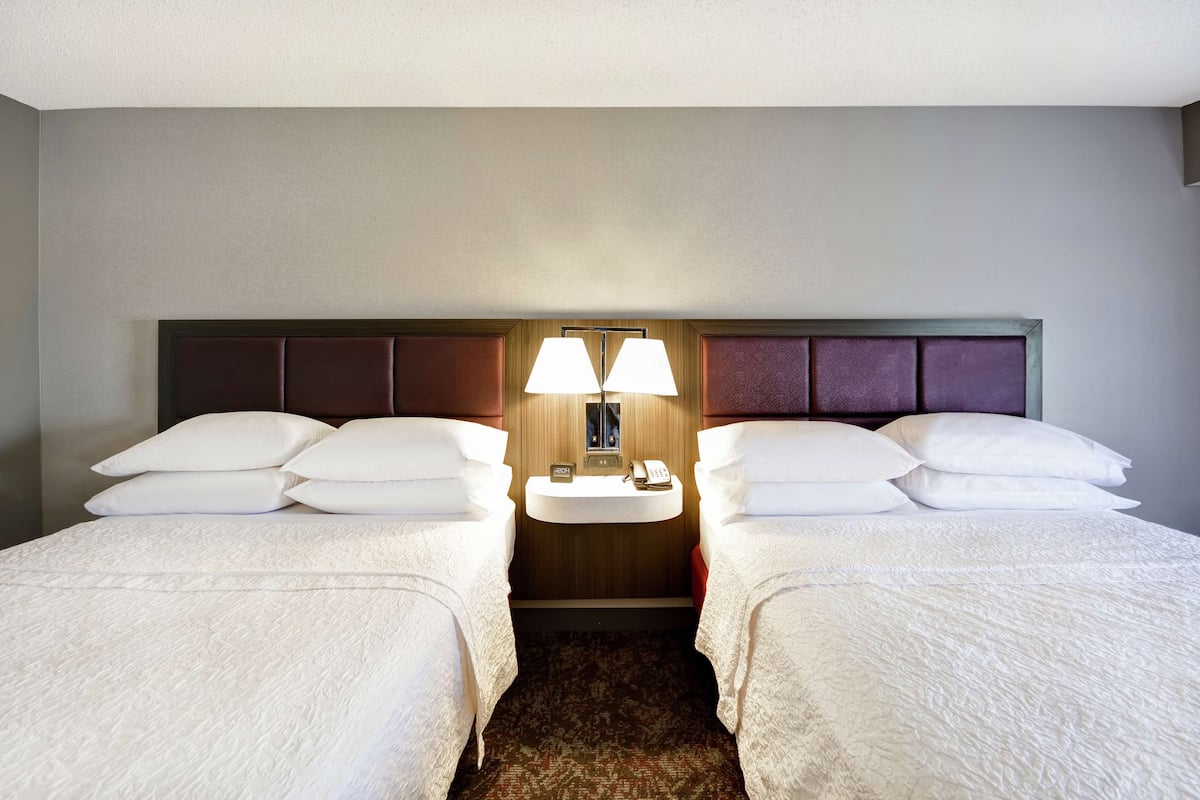 A hotel room with two beds, a bedside table with a lamp, and a small wall-mounted TV.