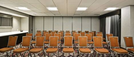 A conference room with rows of orange chairs, a long table, and patterned carpet.