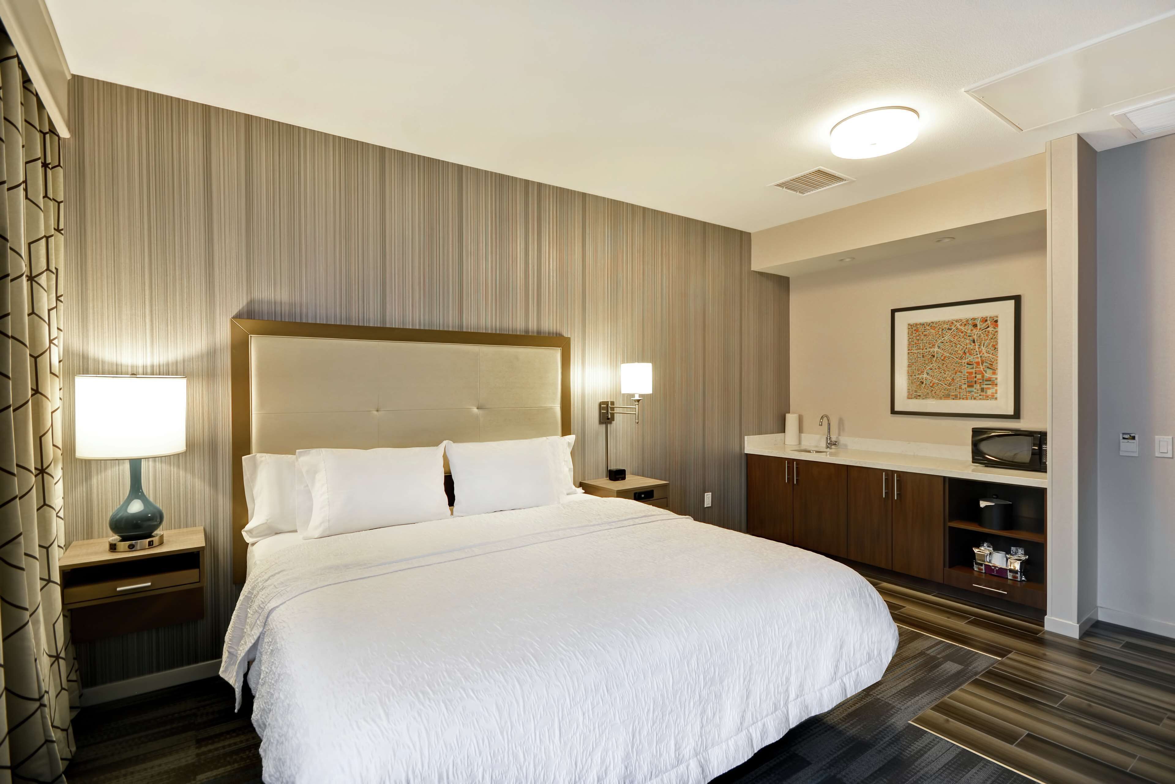 Een hotelkamer met een groot bed, twee nachtkastjes, een dressoir, een magnetron en een lijst aan de muur.