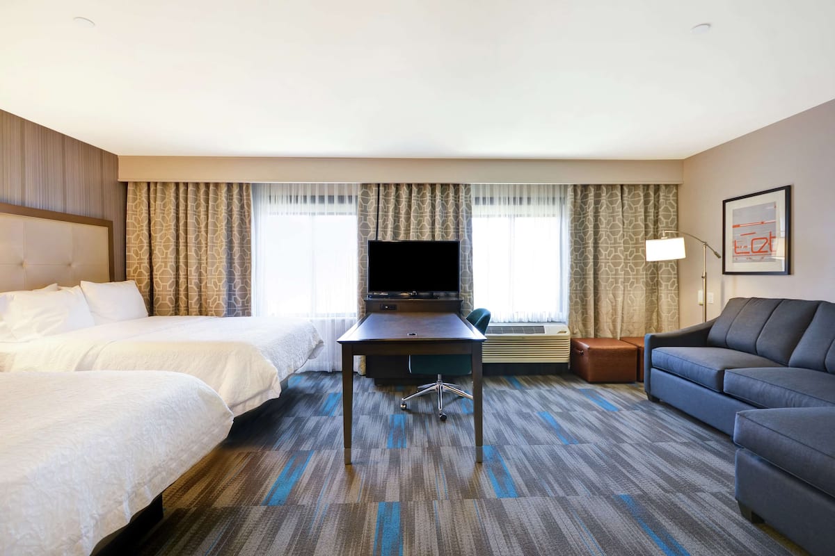 A hotel room with two beds, a desk with a flat-screen TV, a sofa, and a lamp.