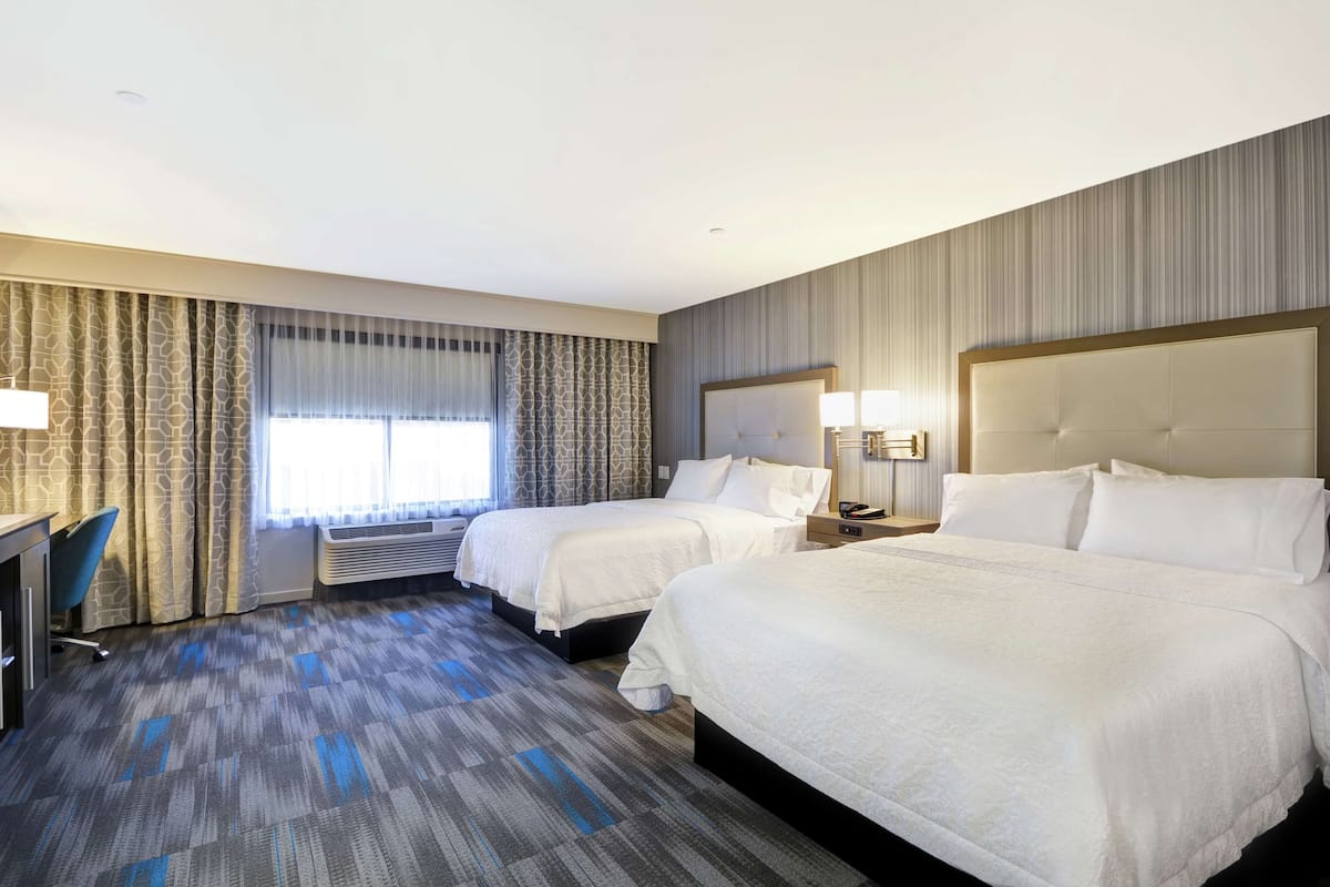 A hotel room with two beds, a desk, and a chair.