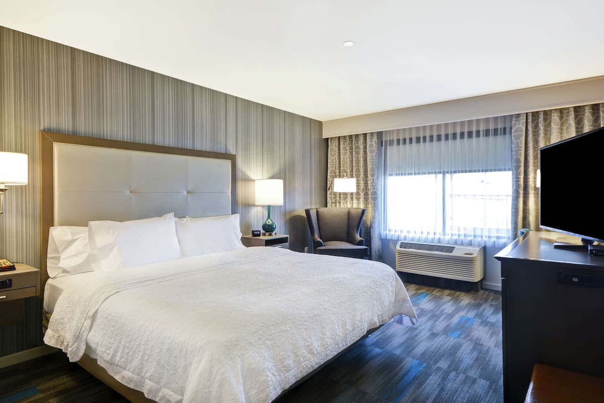 A hotel room with a large bed, a desk, a chair, and a TV.