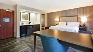 Een hotelkamer met een bed, nachtkastjes, een bureau, een stoel, een kitchenette en een badkamer.