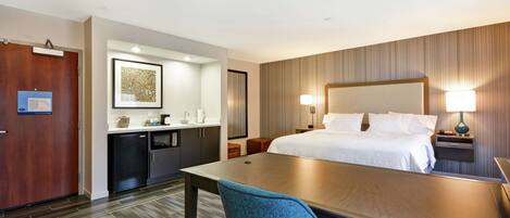 Habitación de hotel con cama, mesitas de noche, escritorio, silla, kitchenette y baño.