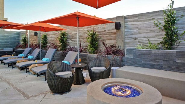 Een terras met lounge stoelen, parasols en een vuurkuil.