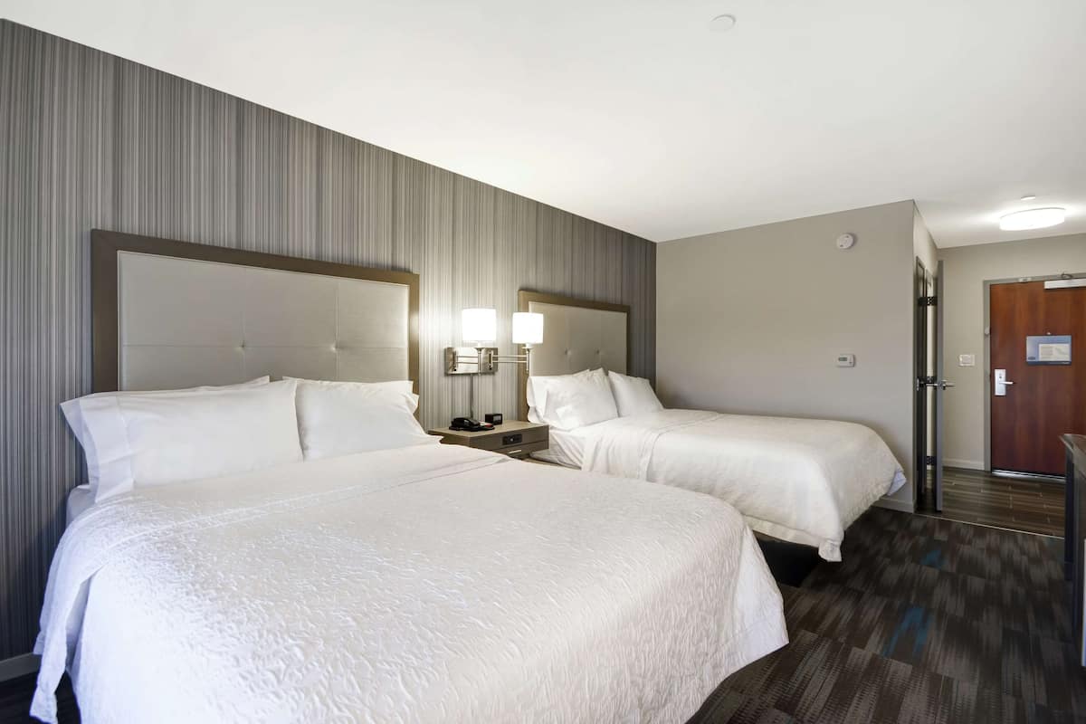 A hotel room with two beds, a nightstand with lamps, and a door to the bathroom.