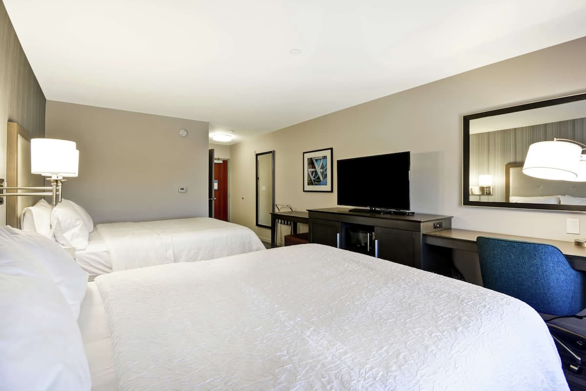 A hotel room with two beds, a desk, a television, and a mirror.