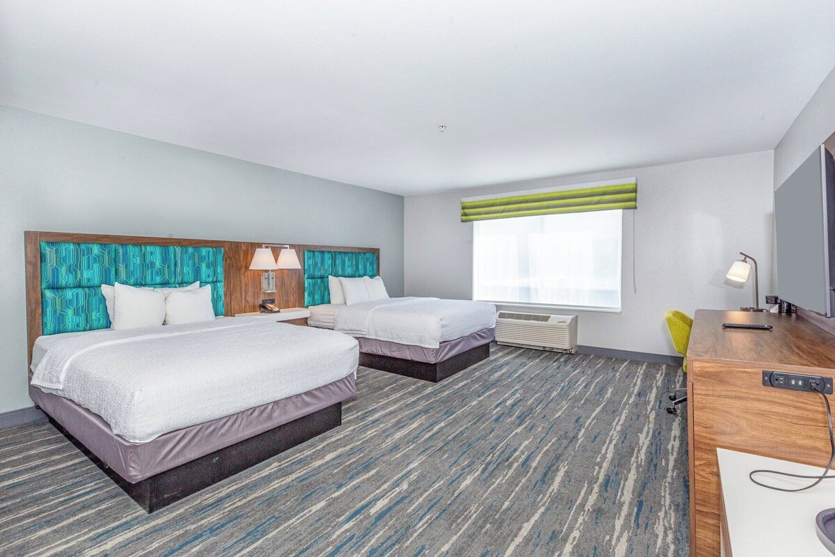 A hotel room with two beds, a desk, a chair, a TV, and a window with blinds.