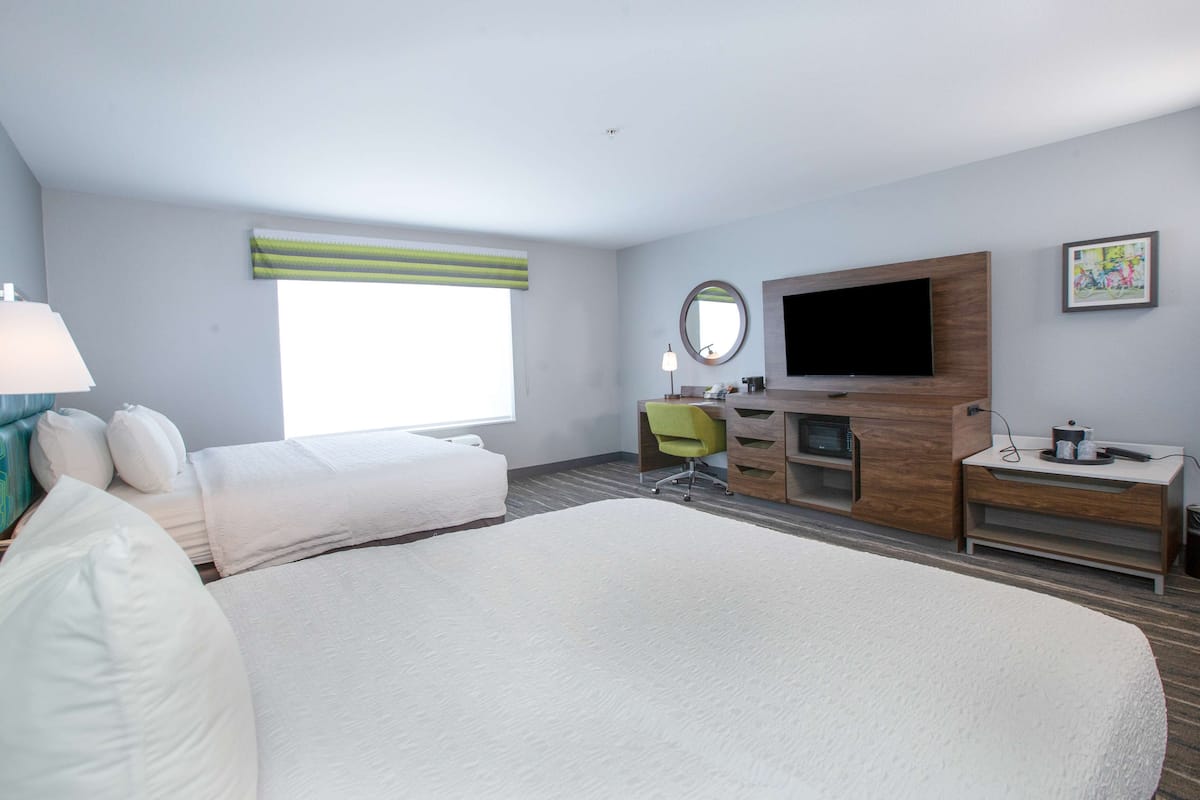 A hotel room with a large bed, a desk, a chair, a TV, and a window with blinds.
