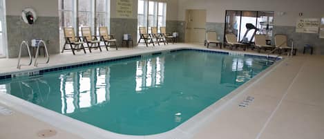 An indoor swimming pool with lounge chairs and safety signs.